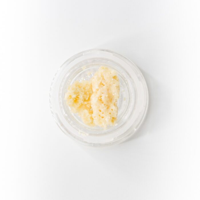 Close-up of White Fire OG Crumble Concentrate Wax from Monster of Terps in a clear container, showcasing its golden, crumbly texture.