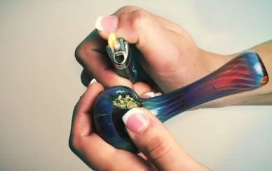 Person demonstrating how to properly pack a bowl using ground cannabis, a grinder, and a glass pipe.